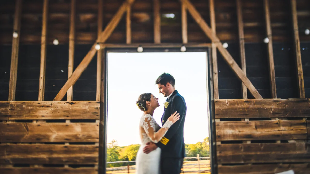 A bride and groom standing in the doorway of a barn.