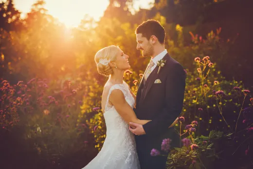 A bride and groom standing in a field at sunset.