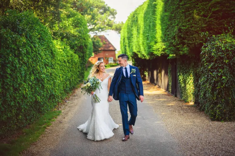 A bride and groom walking down a path surrounded by hedges.