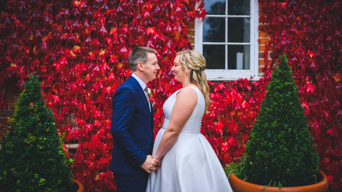 A bride and groom standing in front of a red brick wall.