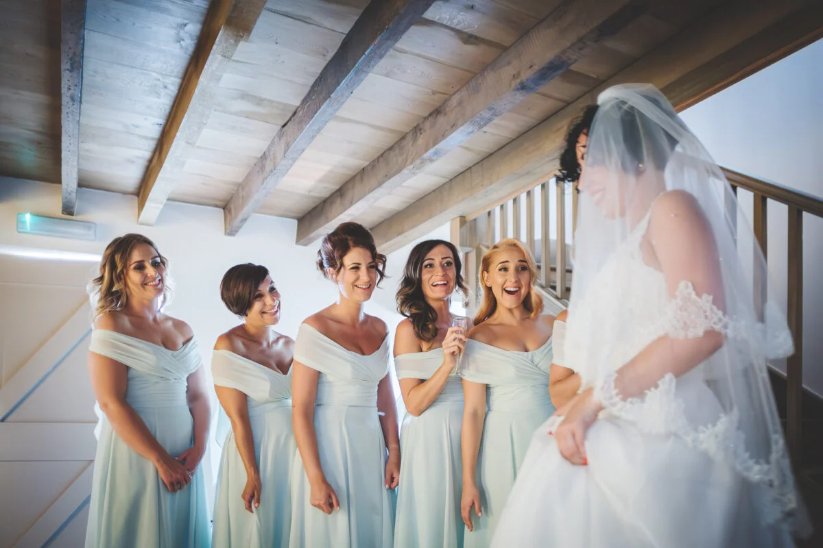 A bride and her bridesmaids look at each other.