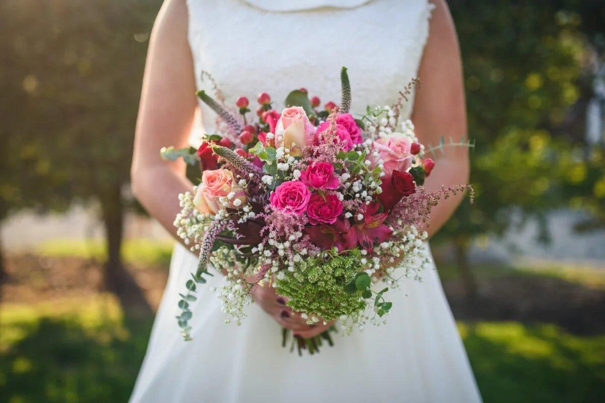 A bride holding a bouquet of pink and green flowers.