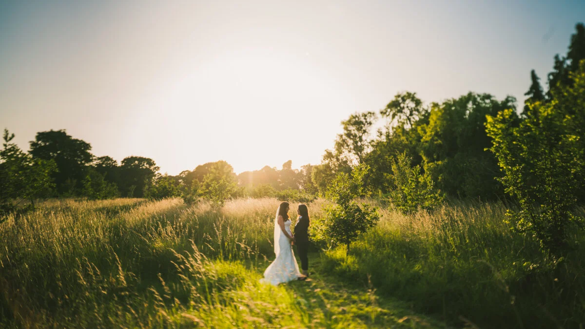A bride and groom standing in a field at sunset.
