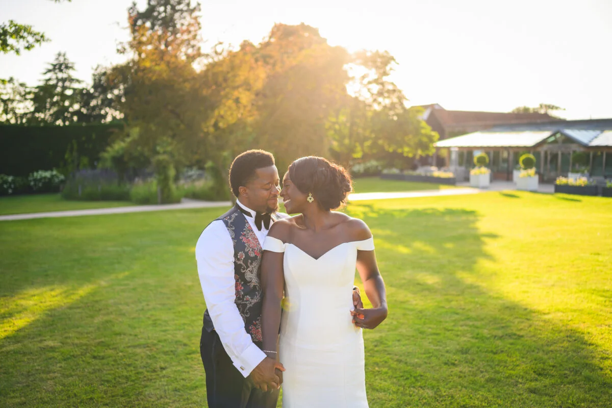 A bride and groom standing in a field at sunset.