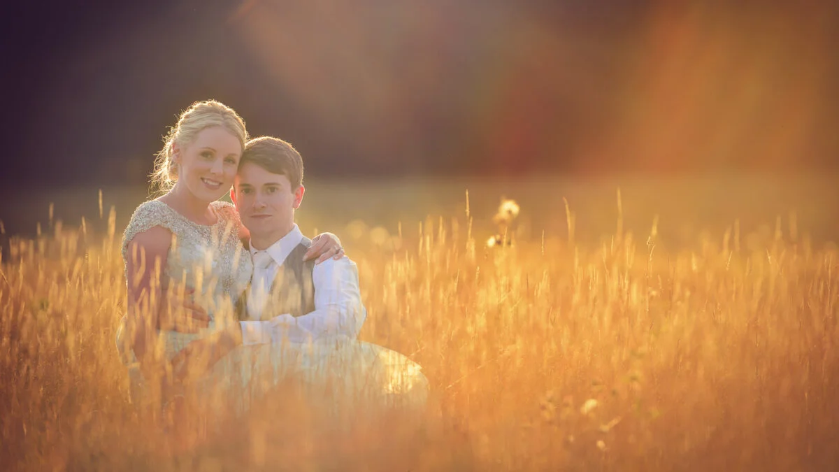 A bride and groom posing in a field of tall grass.