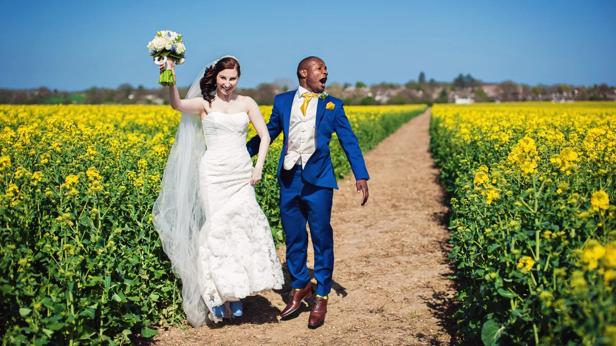 A bride and groom walking through a field of yellow flowers.