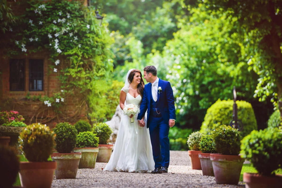 A bride and groom walking through a garden with potted plants.