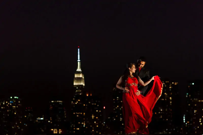 A couple in a red dress standing in front of the empire state building.