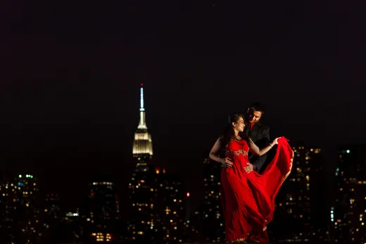 A couple in a red dress standing in front of the empire state building.