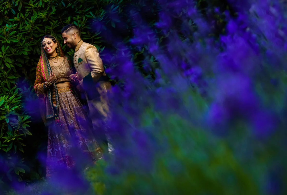 A bride and groom standing in a field of purple flowers.