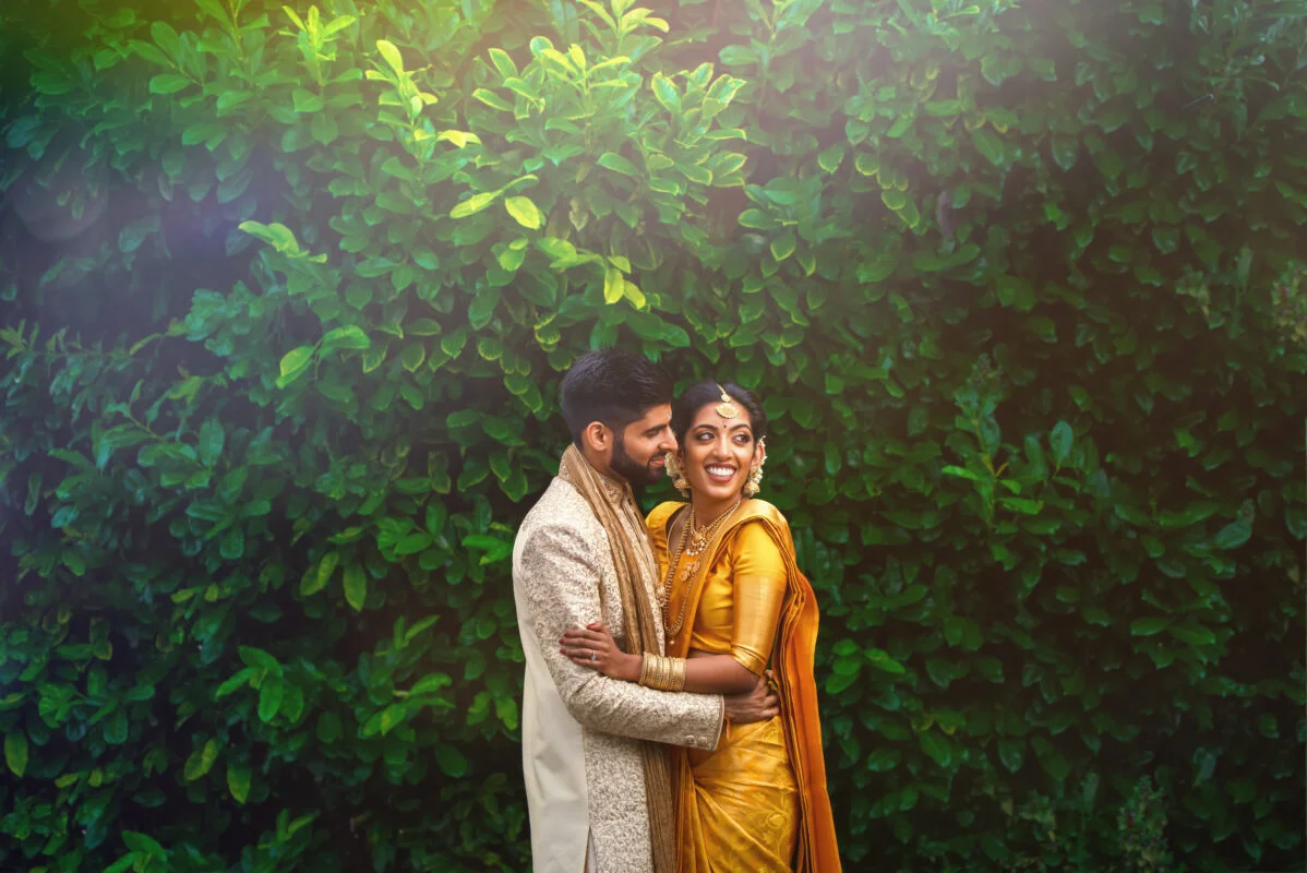An indian couple embracing in front of green foliage.