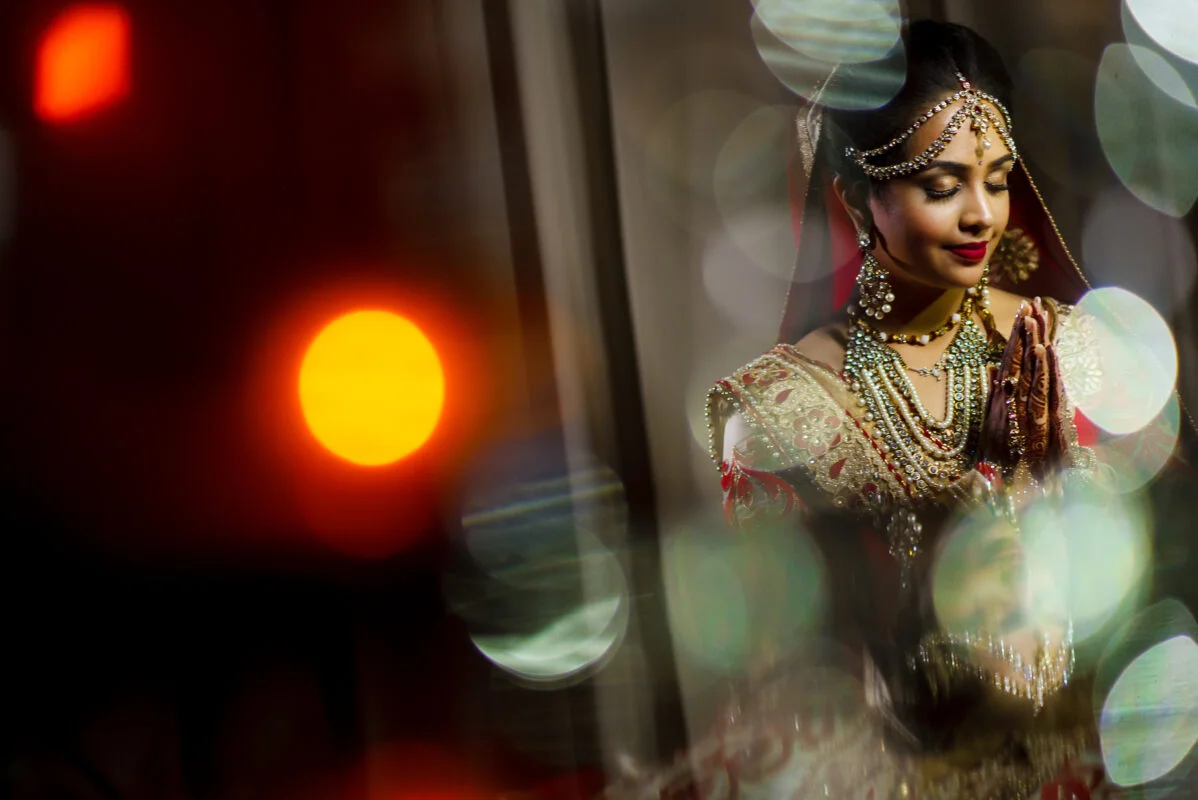 A bride in a traditional indian dress is posing in front of a light.