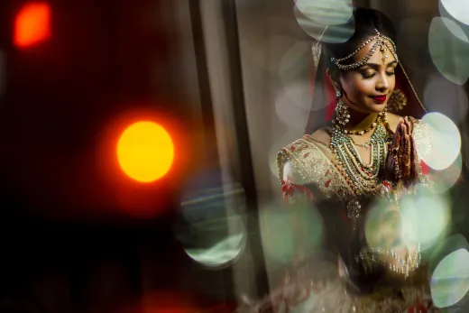 A bride in a traditional indian dress is posing in front of a light.