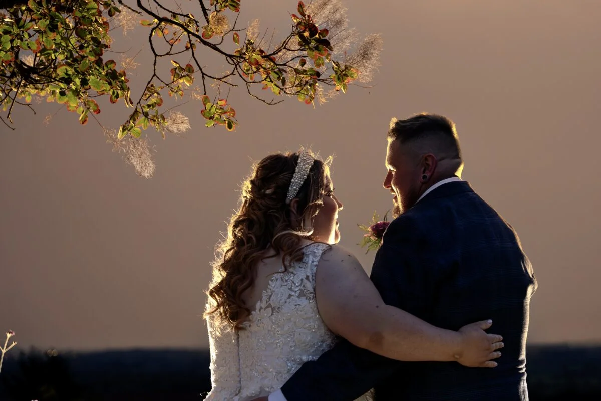 A bride and groom standing under a tree at sunset.