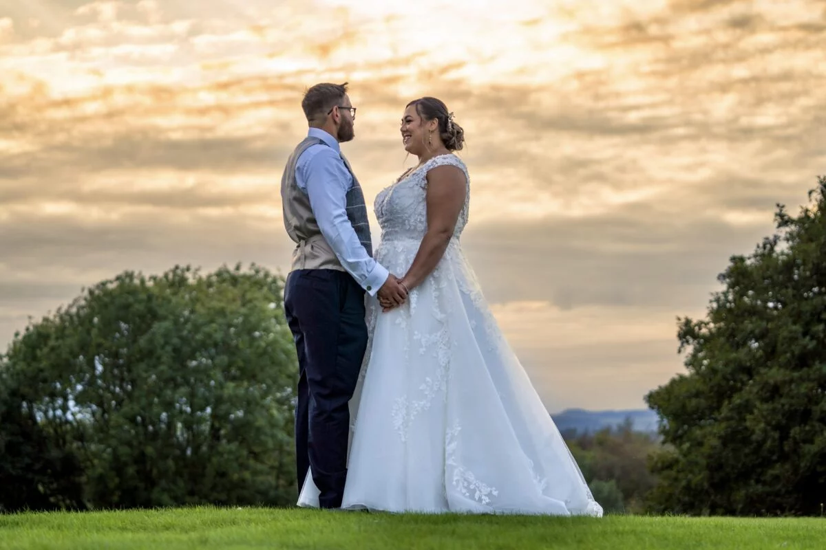 A bride and groom standing in a field at sunset.