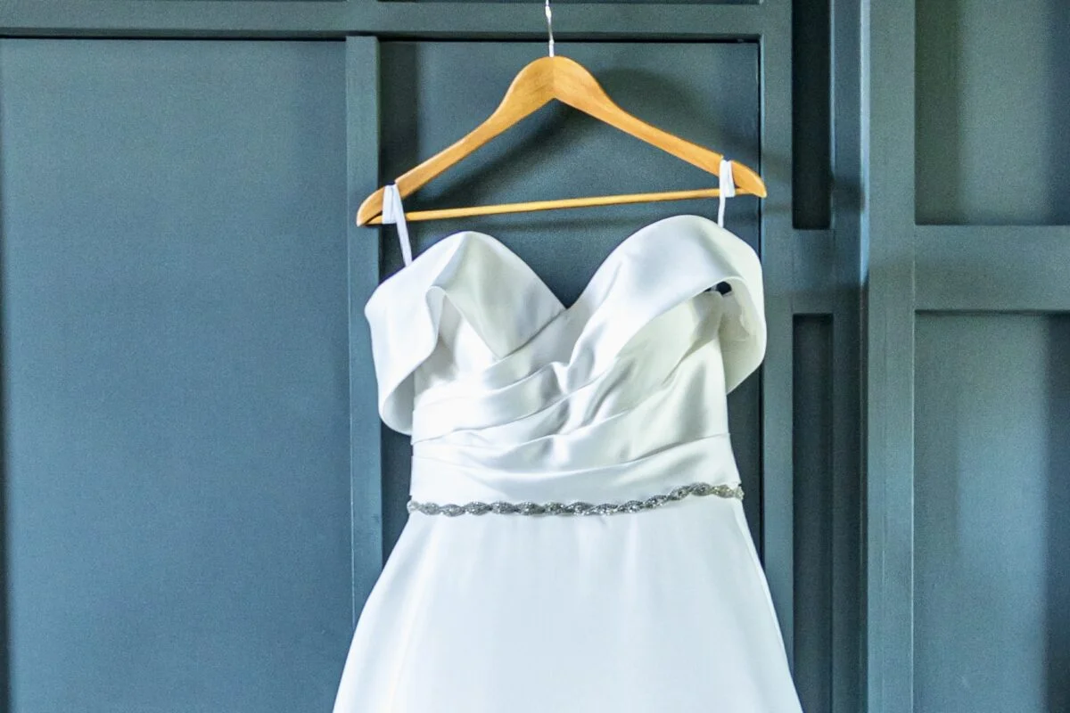 A white wedding dress hanging on a hanger.