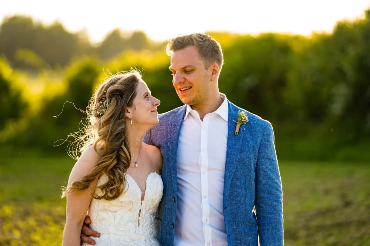 A bride and groom standing in a field at sunset.