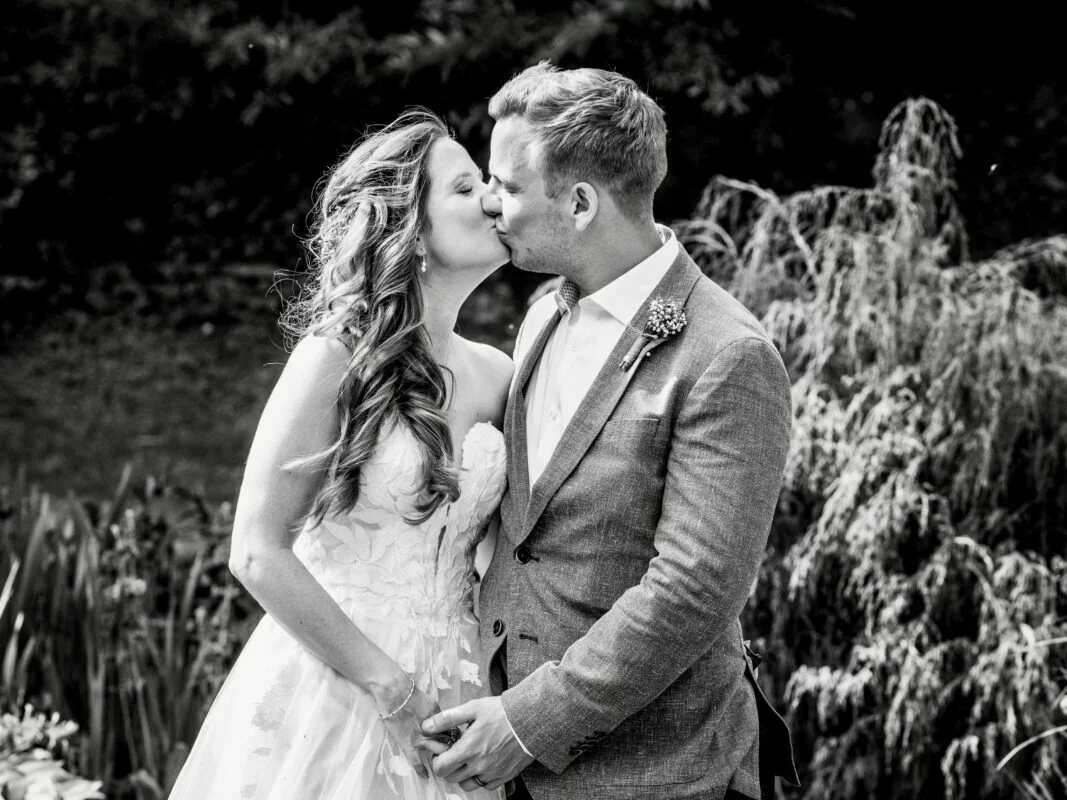A bride and groom kiss in front of a pond.