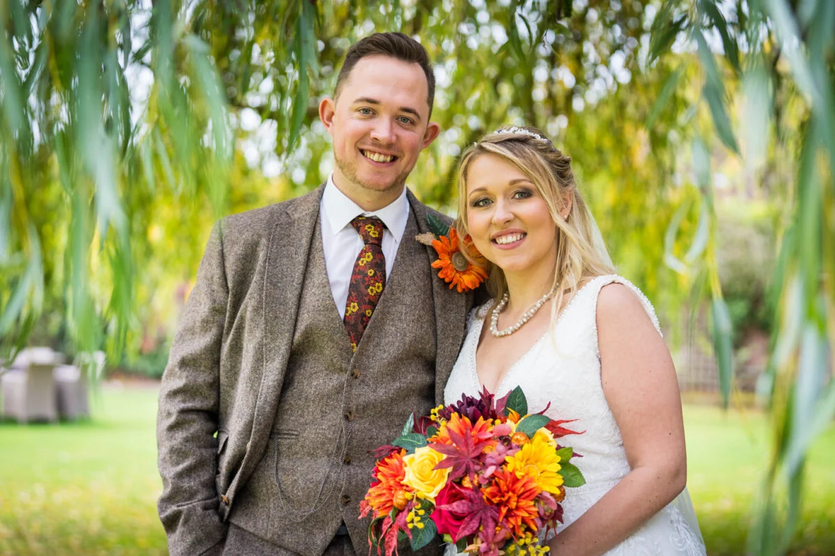 A bride and groom posing under a willow tree.