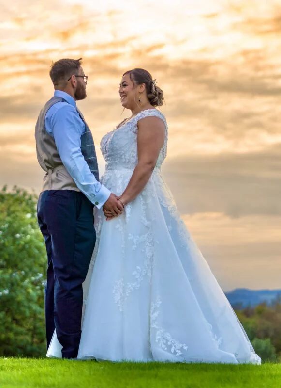 A bride and groom standing in a field at sunset.