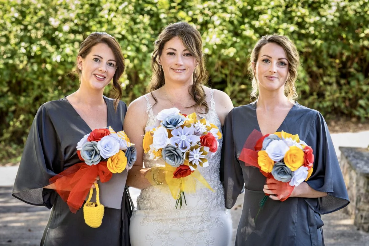 Three bridesmaids holding paper bouquets.