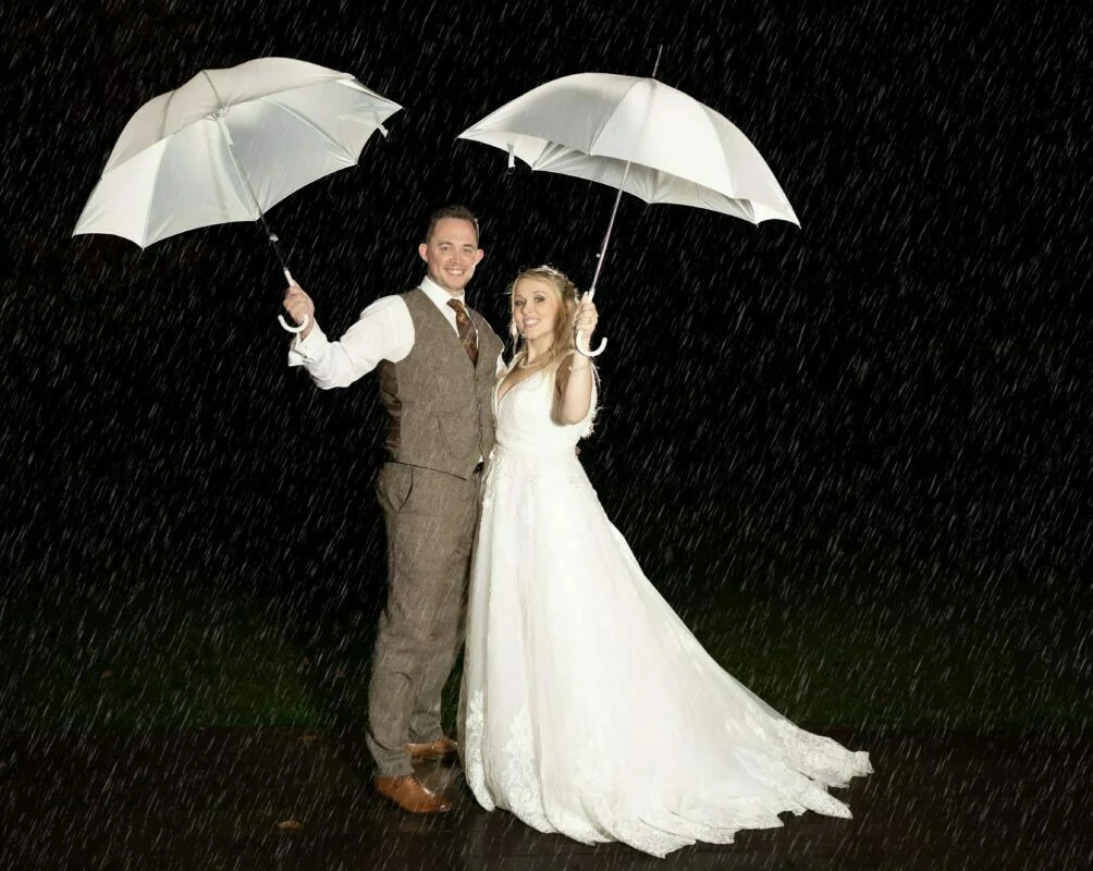 A bride and groom holding umbrellas in the rain.