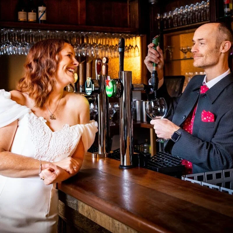 A bride and groom smiling at each other at a bar.