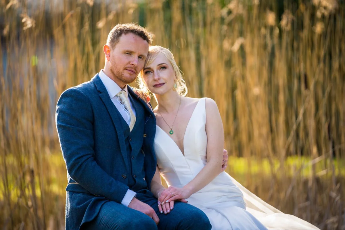 A bride and groom posing in front of tall reeds.
