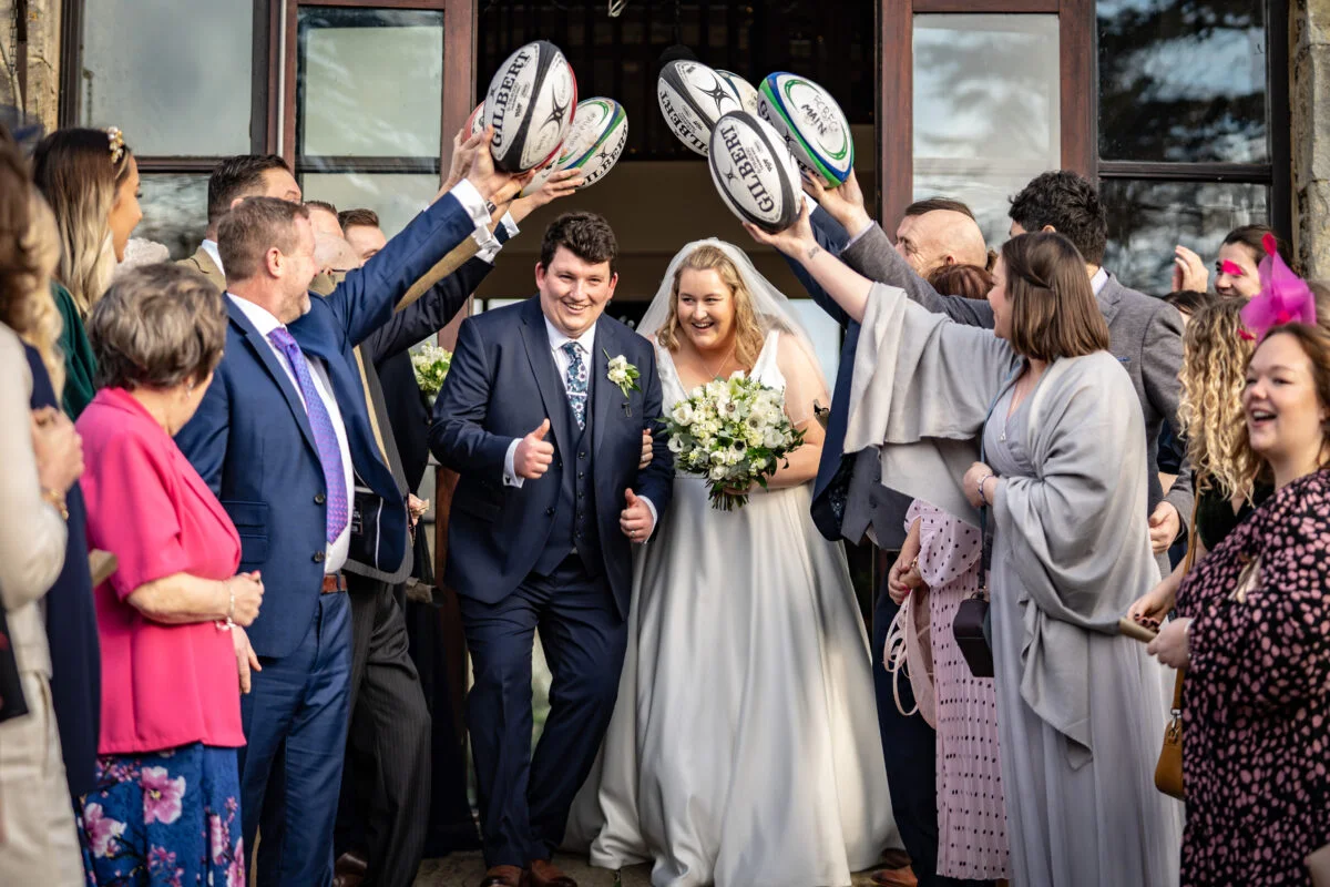 A bride and groom with rugby balls in their hands.