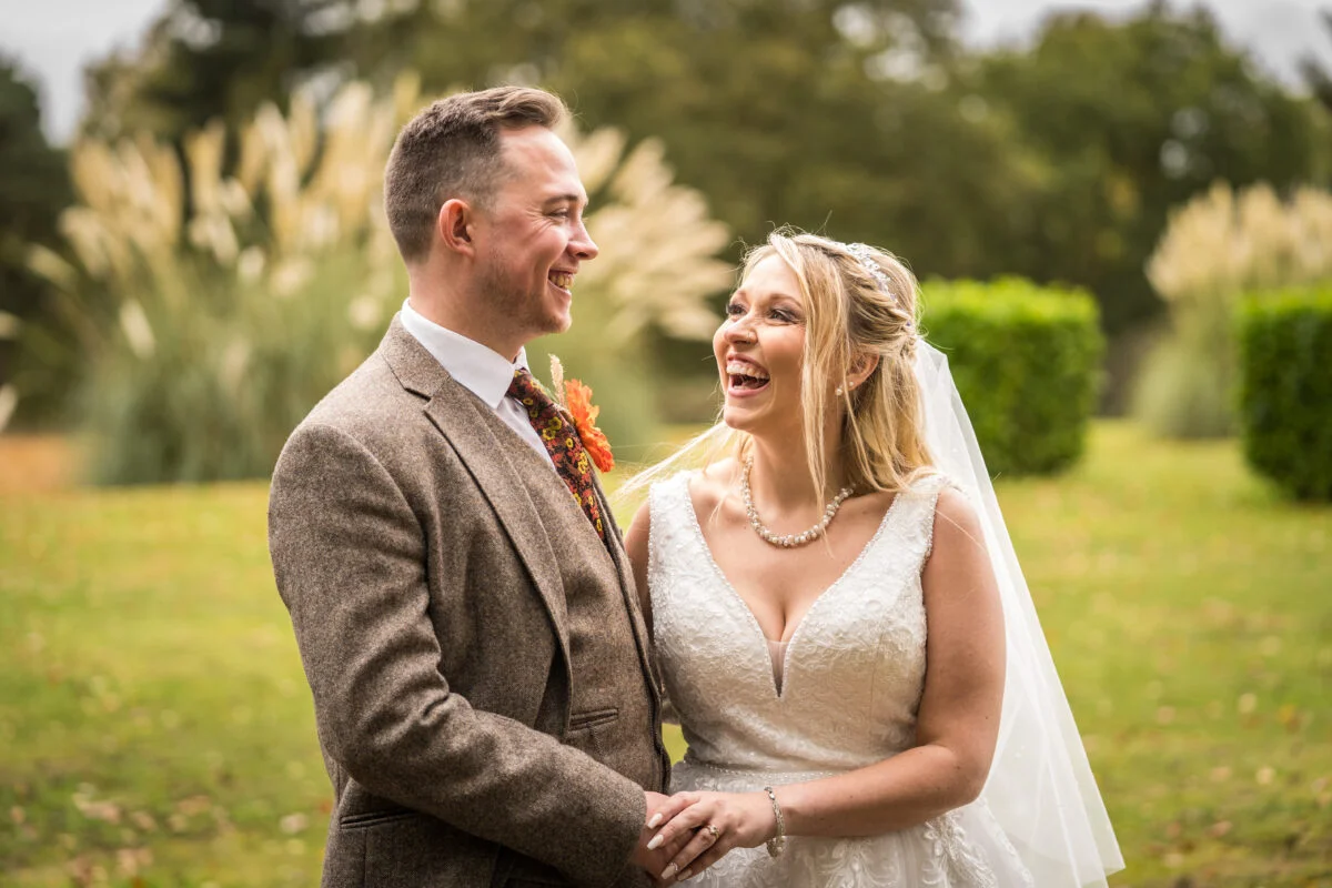 A bride and groom laughing in front of tall grasses.