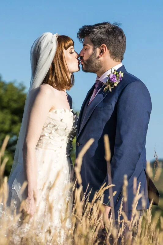A bride and groom kissing in a field of tall grass.