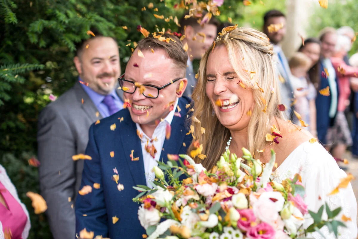 A bride and groom laughing as confetti is thrown at them.