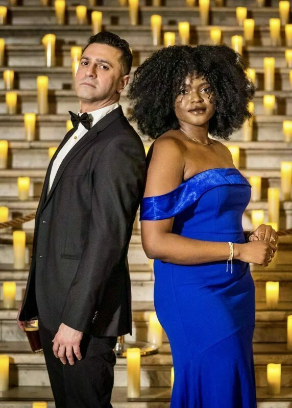 A man and woman in a blue dress standing next to candles.