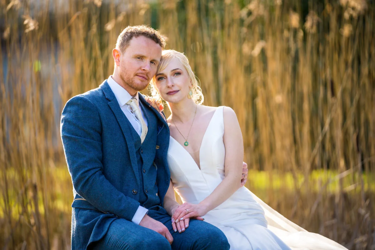 A bride and groom posing in front of tall reeds.
