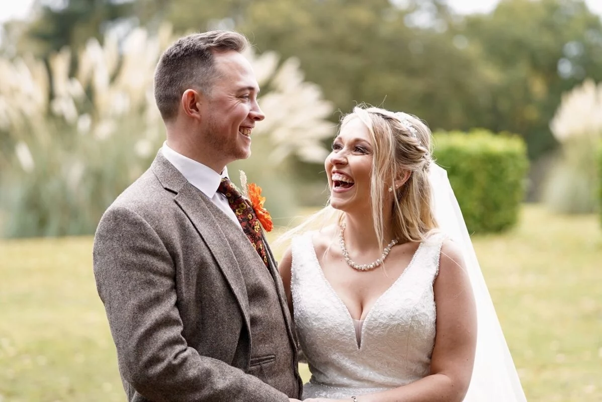 A bride and groom laughing in a field.