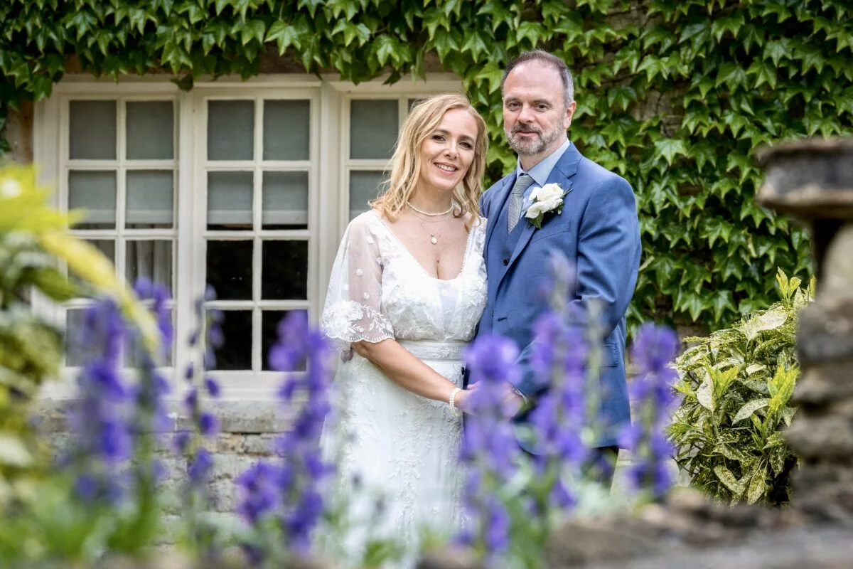A bride and groom posing in front of flowers.