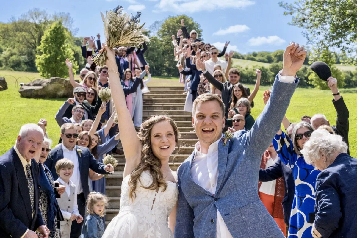 A bride and groom waving to the crowd at their wedding.