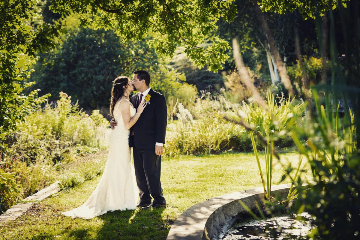 A bride and groom standing in a garden near a pond.