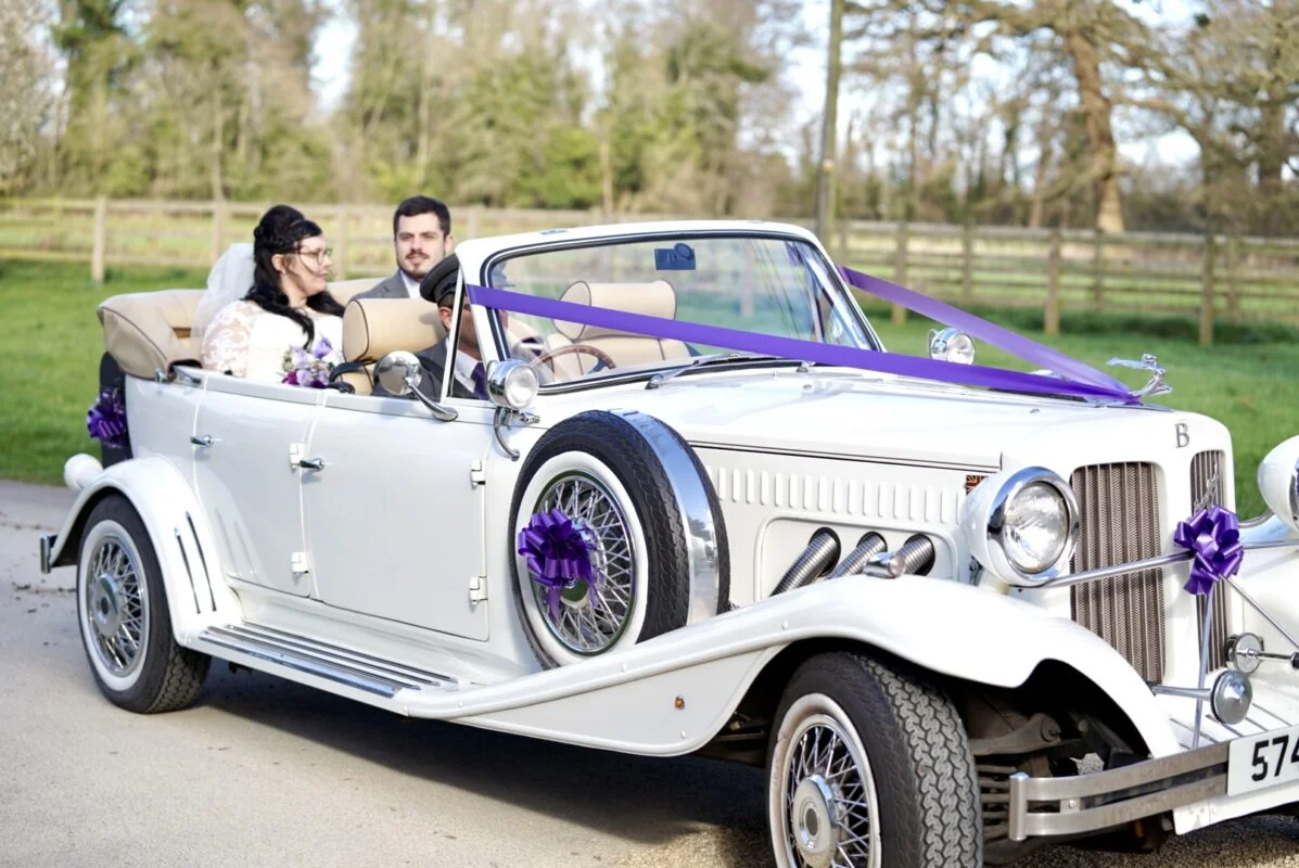 A bride and groom in a white wedding car.
