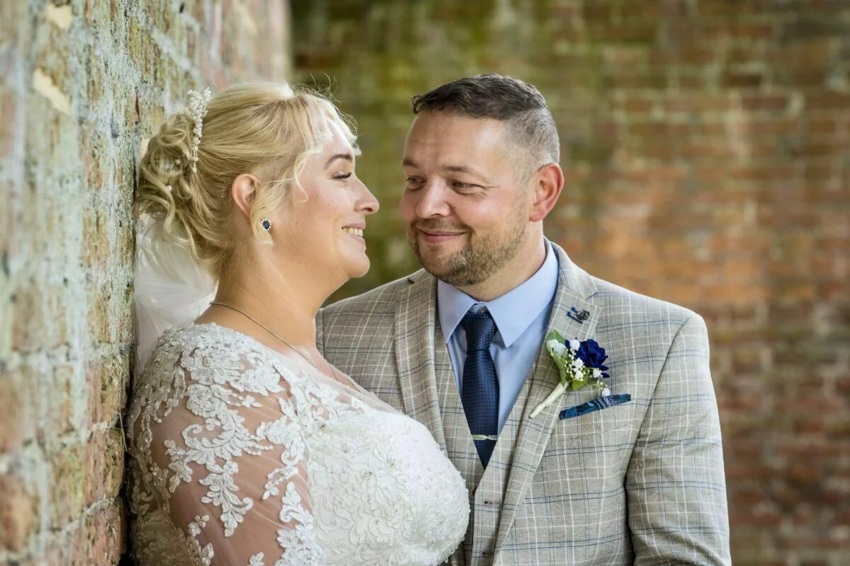 A bride and groom leaning against a brick wall.
