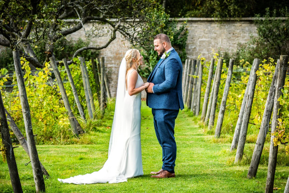 A bride and groom standing in a vineyard.