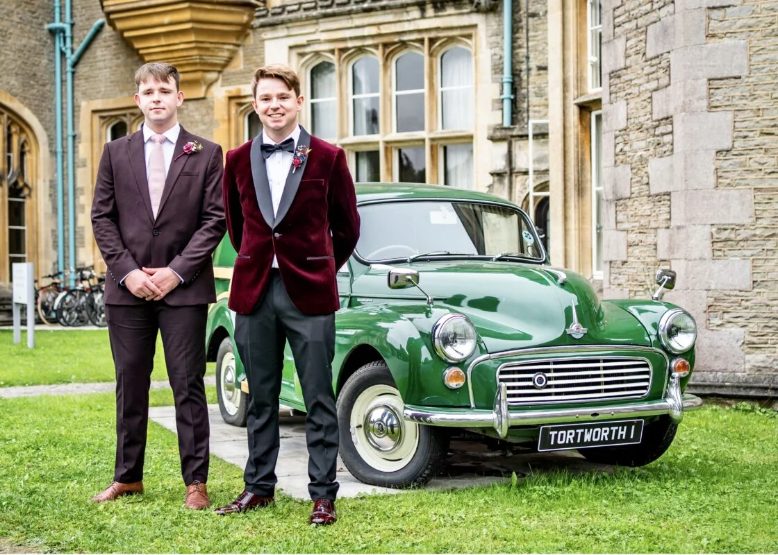 Two men standing next to a green car in front of a castle.