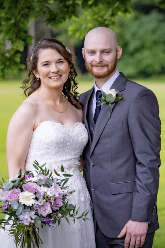 A bride and groom posing for a photo in a park.