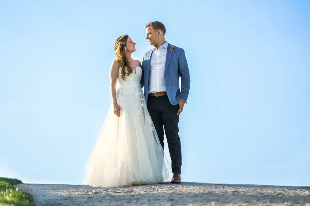 A bride and groom standing on a dirt road.