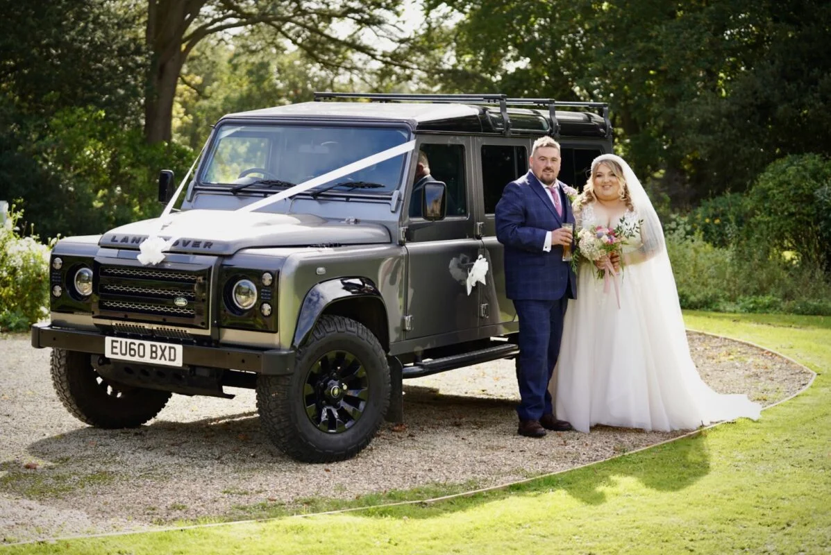 A bride and groom standing next to a land rover.