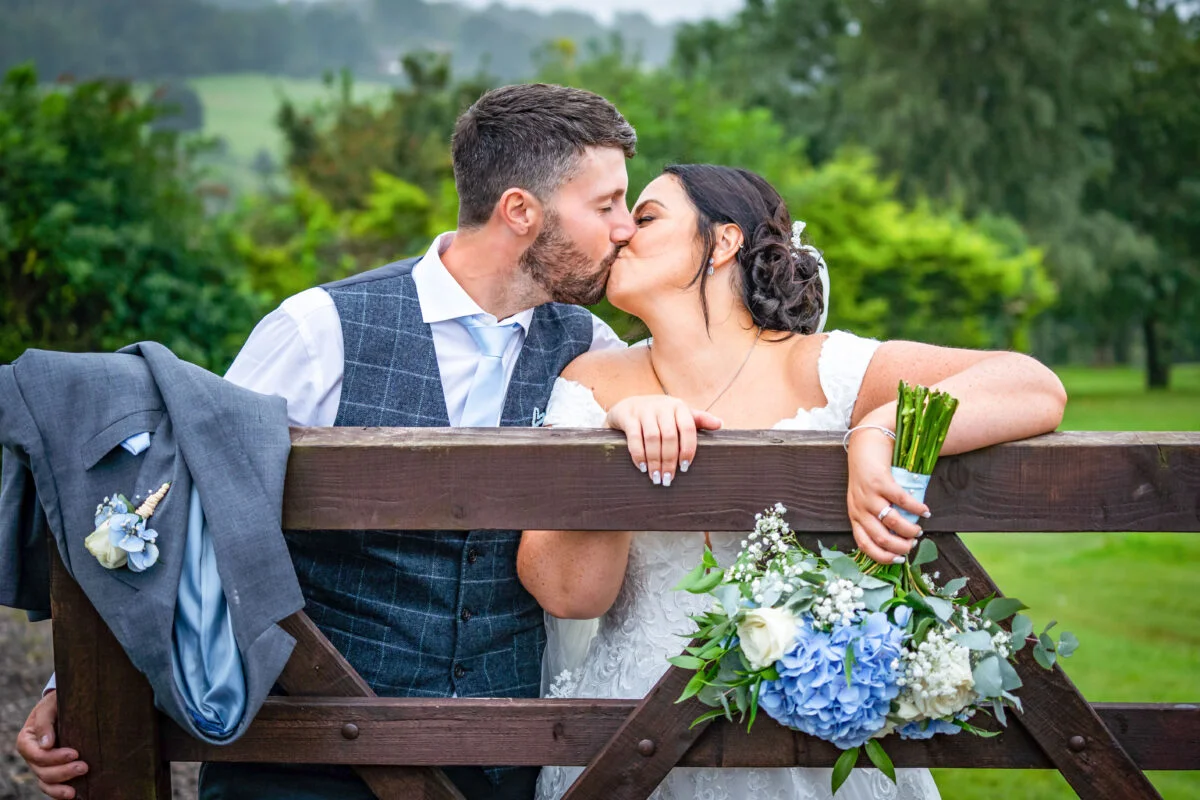 A bride and groom kissing on a wooden fence.