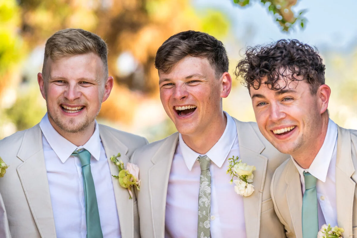 A group of groomsmen in tan suits laughing.