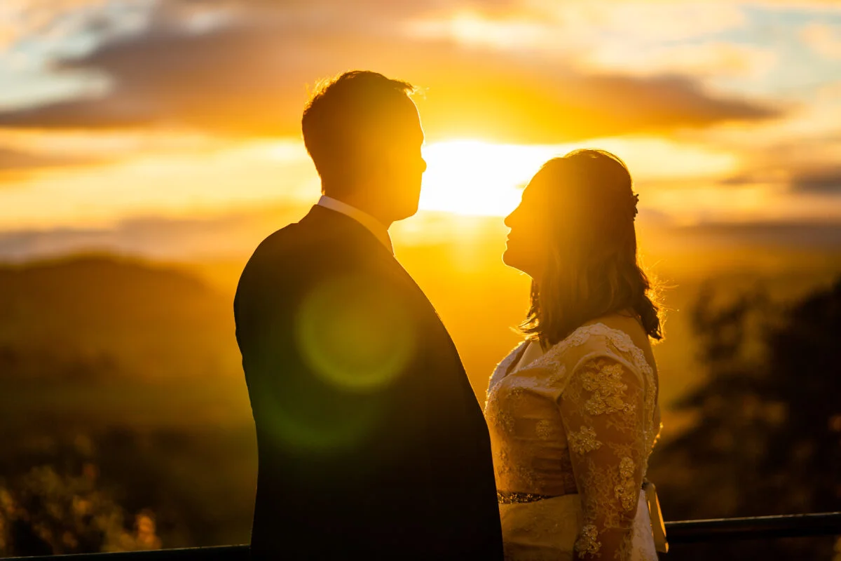 A bride and groom standing in front of a sunset.