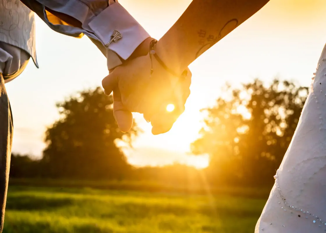 A bride and groom holding hands in a field at sunset.