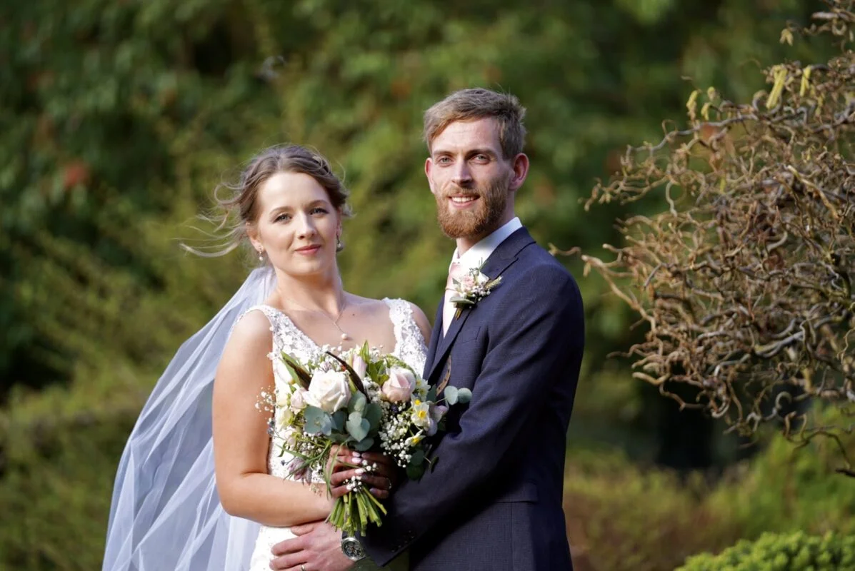 A bride and groom posing for a photo in a garden.